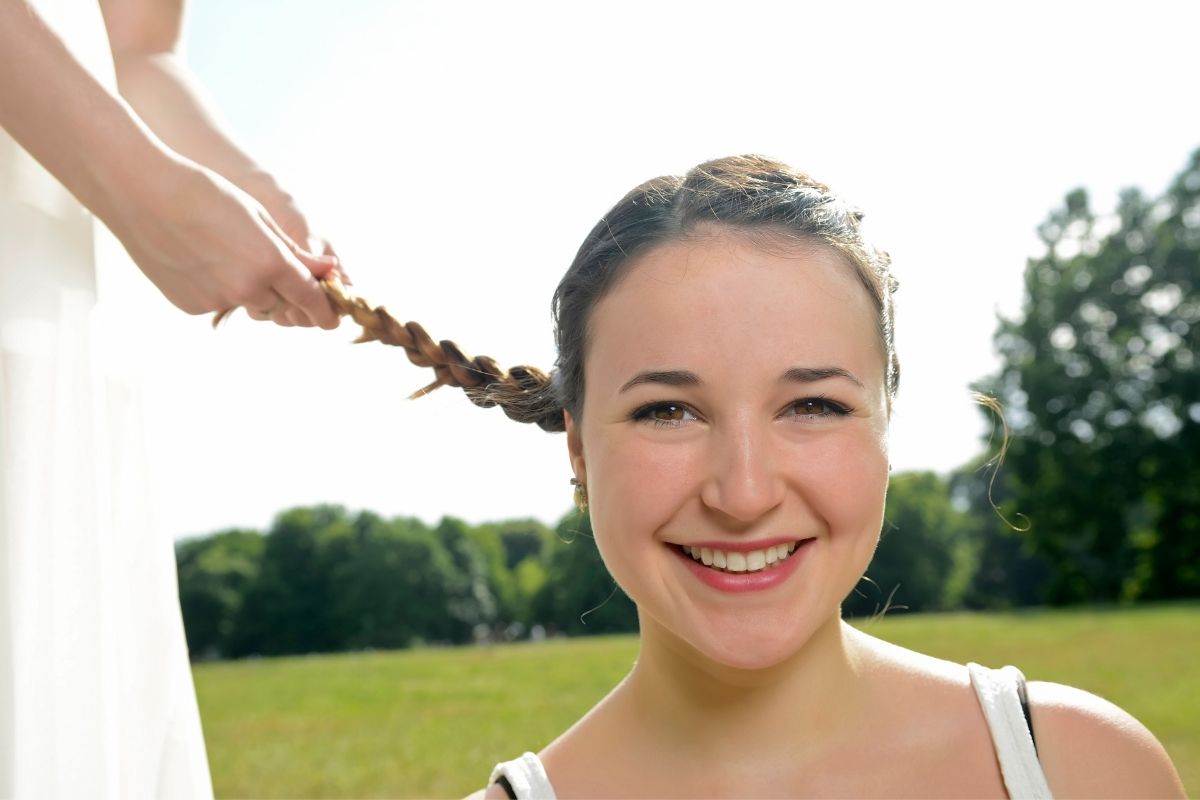 A woman smiling in a green field with a braid.
