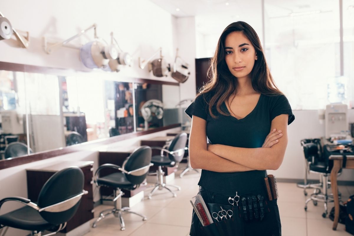 Young lady hairstylist standing near salon chairs