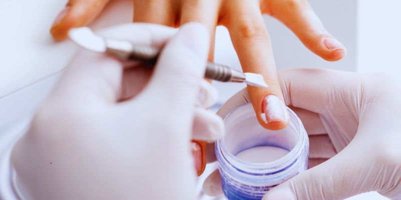 Nail technician demonstrating how to remove SNS at home, with a hand being prepped and dipped powder gently filed before removal.