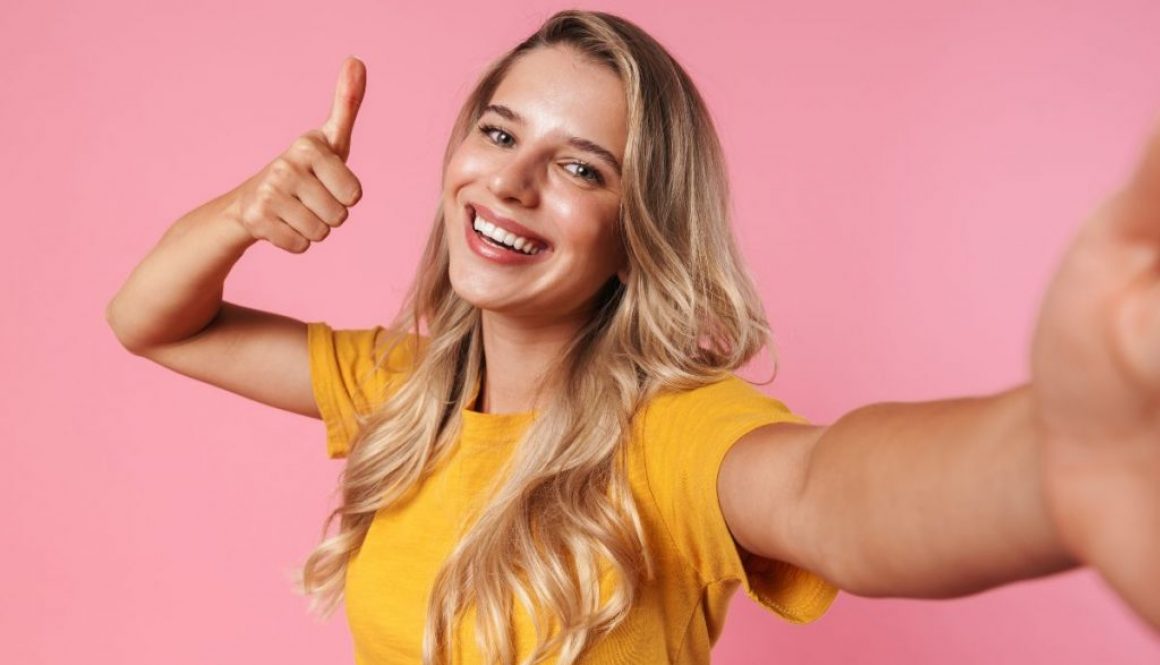 a woman with the right thumbs up taking a selfie in a pink wall