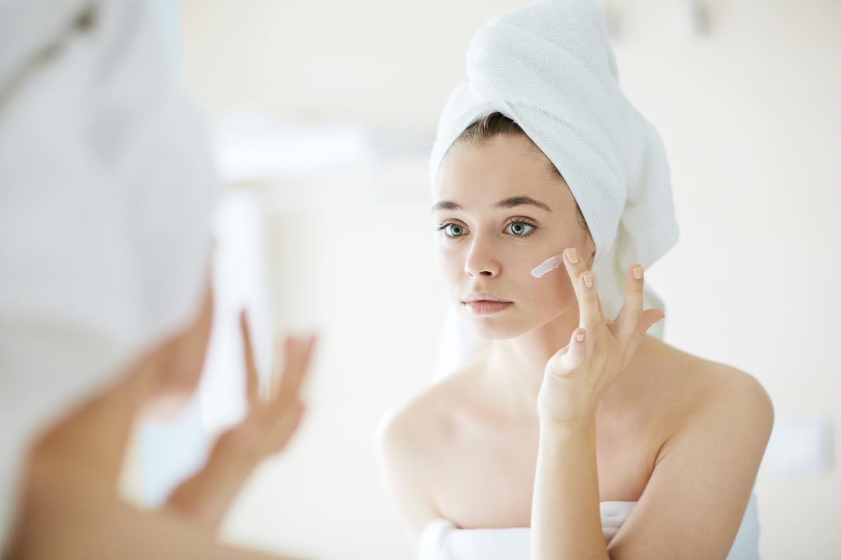 A woman putting on skin moisturizer.