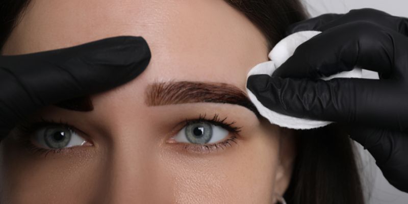 The professional wipes off excess eyebrow tint from the client's eyebrows.