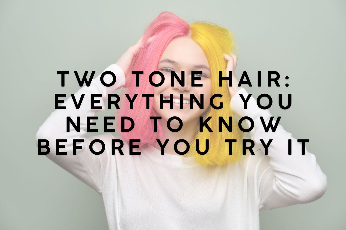 Smiling woman showcasing two tone hair in bright pink and yellow, posing with hands in her hair against a light green background, wearing a cream sweater.