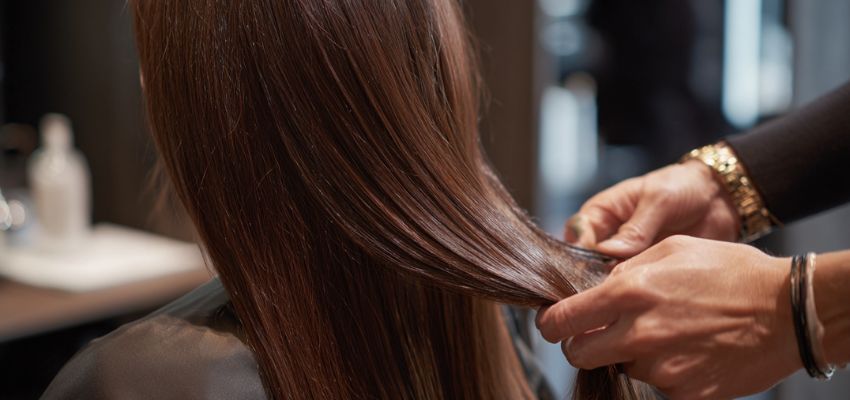 Close-up of hairstylist’s hands carefully installing weft hair extensions, explaining what are weft hair extensions